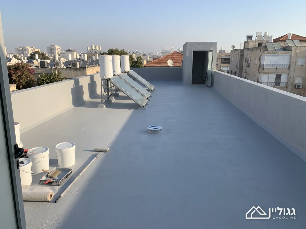גג שטוח מצופה באפור אחיד ומט, עם עליית ציפוי על המעקה, דודי שמש, פתח ניקוז פתוח ודליים ורולר מונחים בצד, באור נמוך מהצד.
